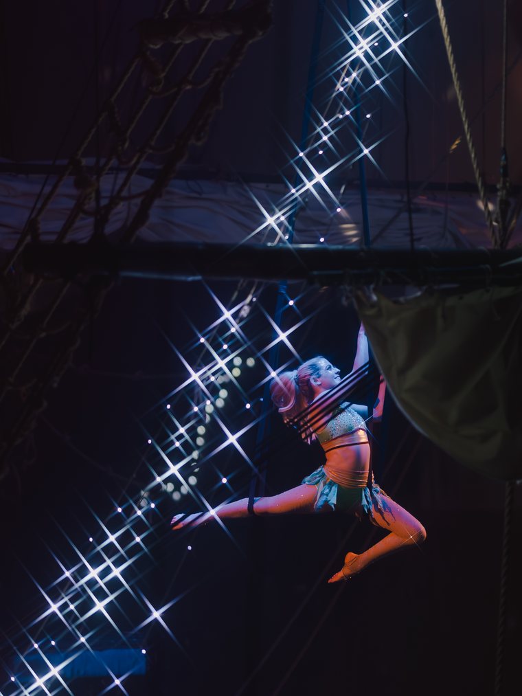 An aerial performer suspended in the rigging mid-routine above the ship