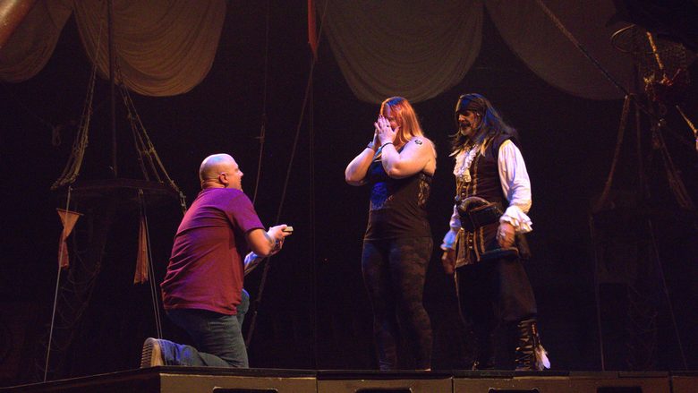 Two adult guests laugh on stage alongside pirate performers