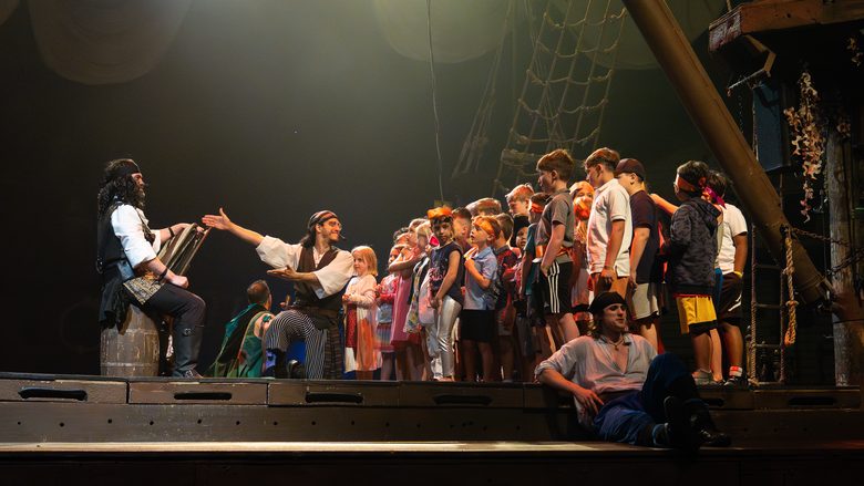 A pirate performer welcomes a line of children up onto the stage