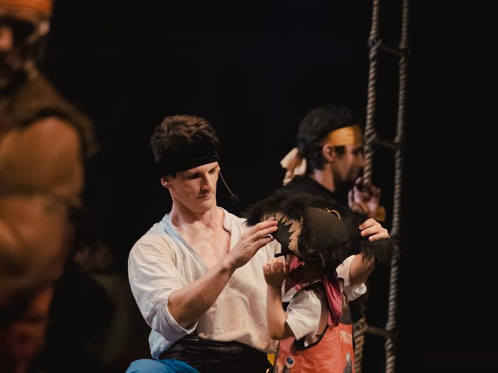 A performer helps a young guest try on a pirate hat on stage