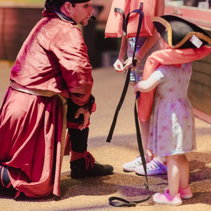 A costumed pirate kneels to greet two young guests in life vests