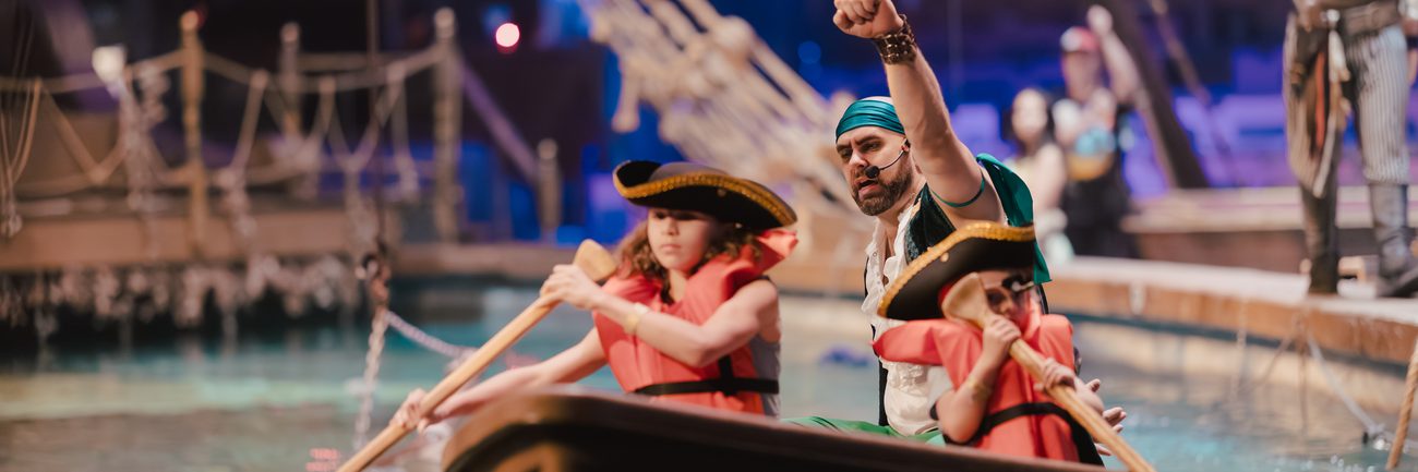 A pirate rows a boat with two cheering children across the indoor lagoon